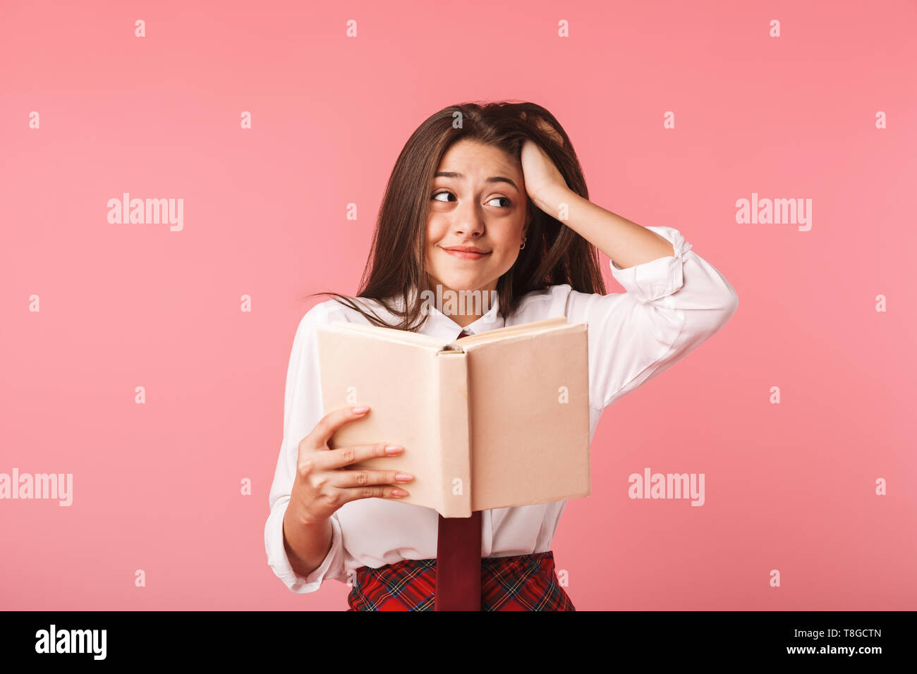 Ritratto di ragazza caucasica 15-16y in uniforme scolastica libro di lettura permanente, mentre isolate su sfondo rosso Foto Stock