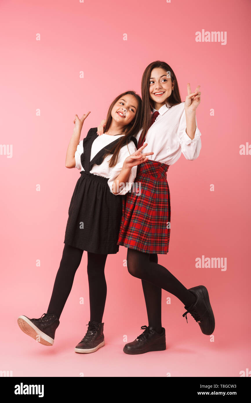 Due allegro scuola ragazze indossano uniformi isolato permanente su sfondo rosa Foto Stock