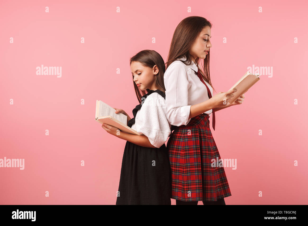 Due allegro scuola ragazze indossano uniformi isolato permanente su sfondo rosa, tenendo i libri Foto Stock