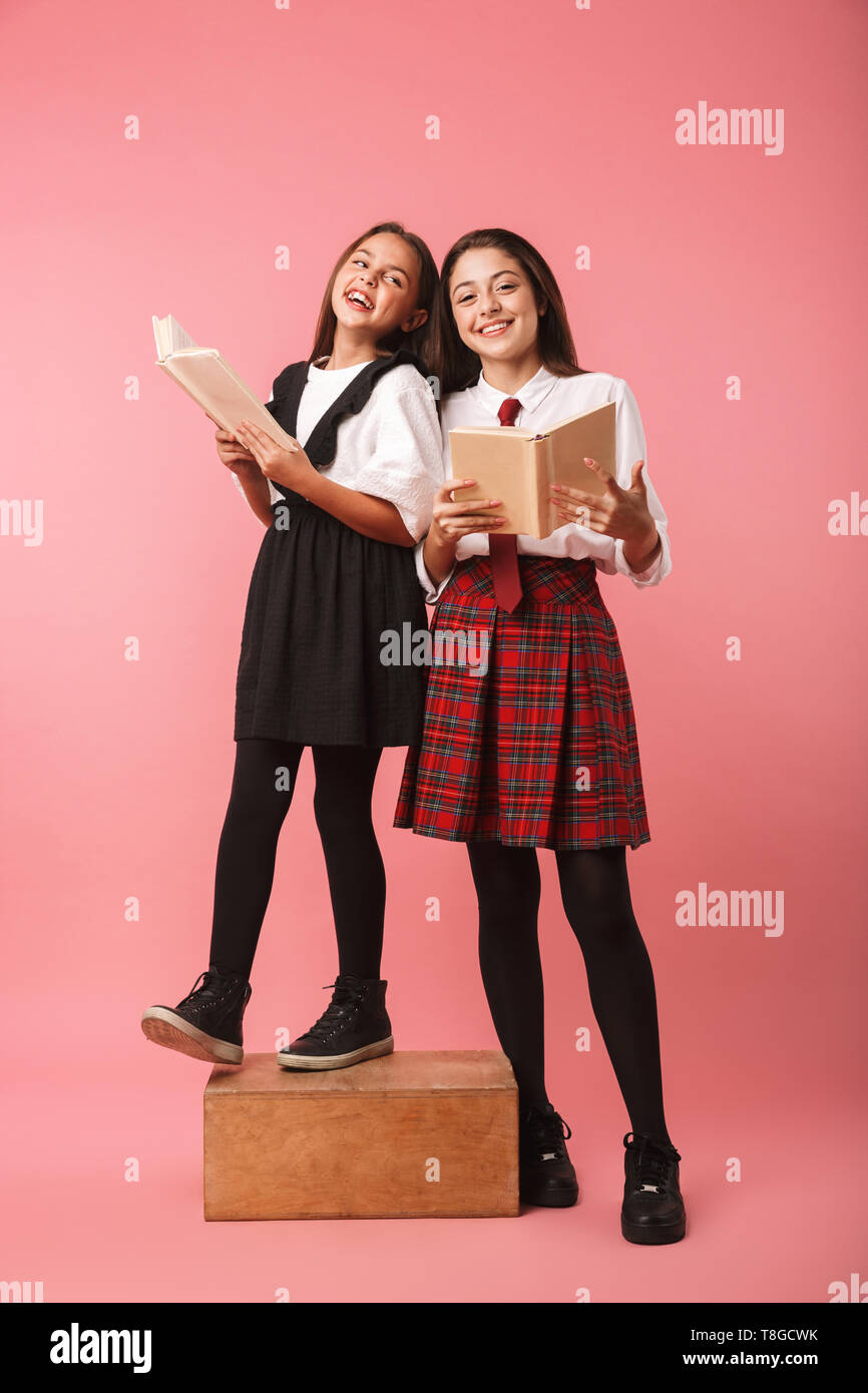 Due allegro scuola ragazze indossano uniformi isolato permanente su sfondo rosa, tenendo i libri Foto Stock
