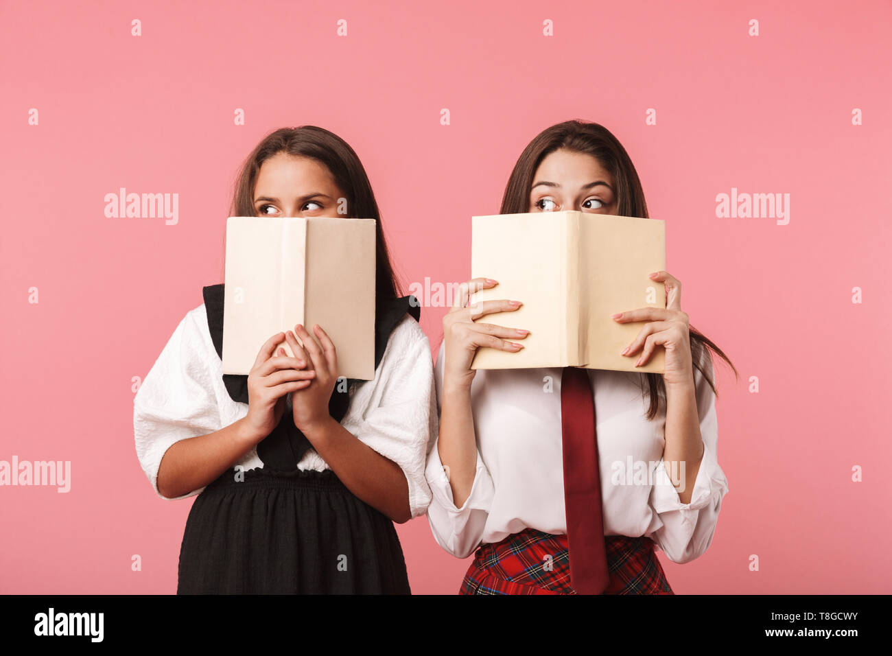 Ritratto di funny ragazze in uniforme scolastica libri di lettura permanente, mentre isolate su sfondo rosso Foto Stock