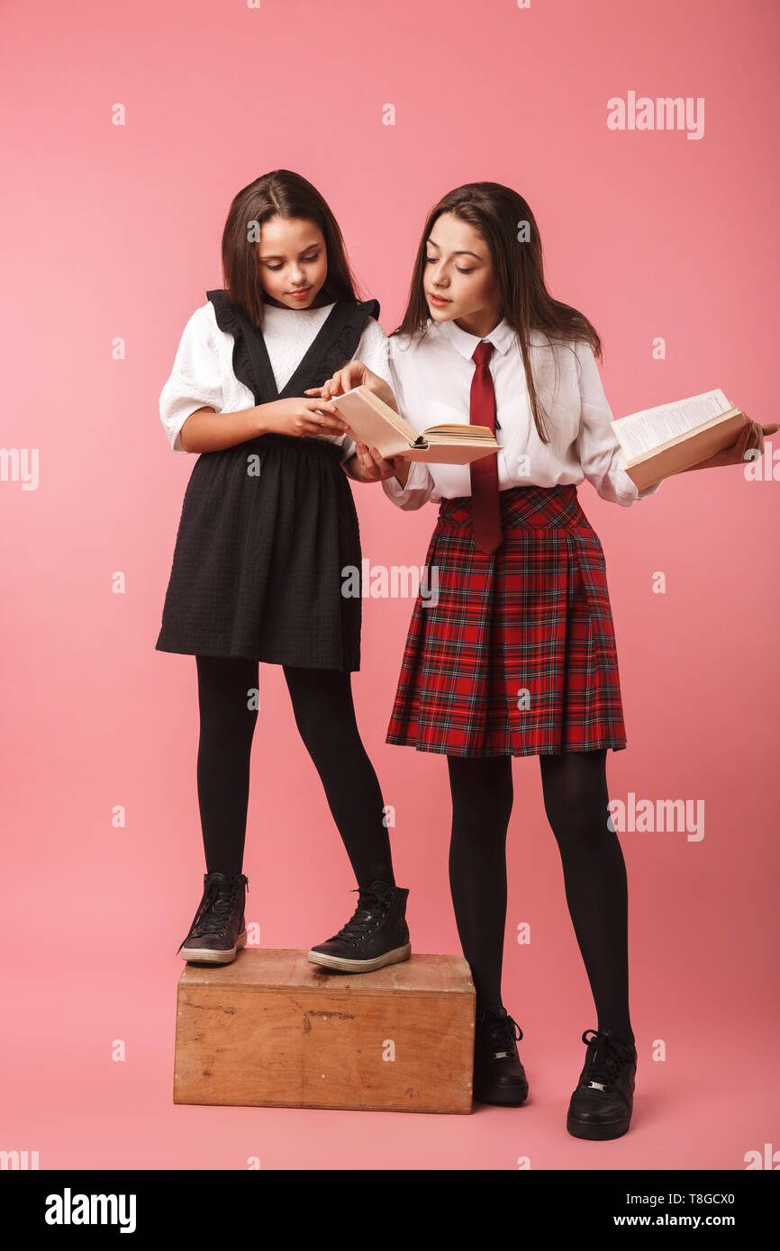 Ritratto di ragazze positivo in uniforme scolastica libri di lettura permanente, mentre isolate su sfondo rosso Foto Stock
