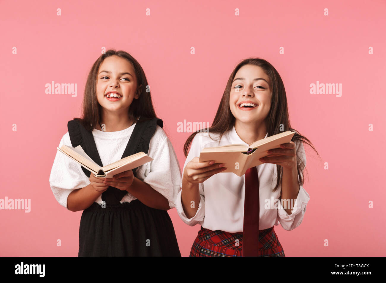 Ritratto di adorabili ragazze in uniforme scolastica libri di lettura permanente, mentre isolate su sfondo rosso Foto Stock