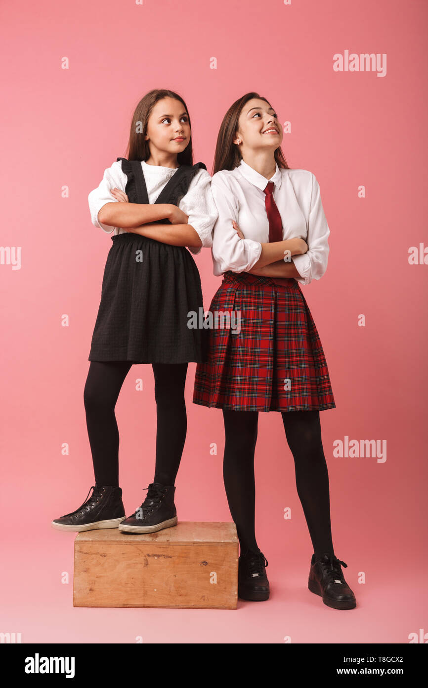 Ritratto di ragazze caucasiche in uniforme scolastica in piedi isolato su sfondo rosso Foto Stock