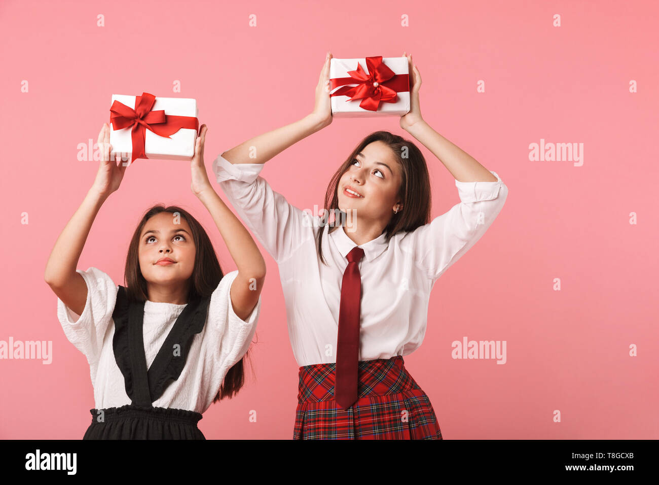 Ritratto di lieta ragazze in uniforme scolastica tenendo presente le caselle mentre in piedi isolato su sfondo rosso Foto Stock