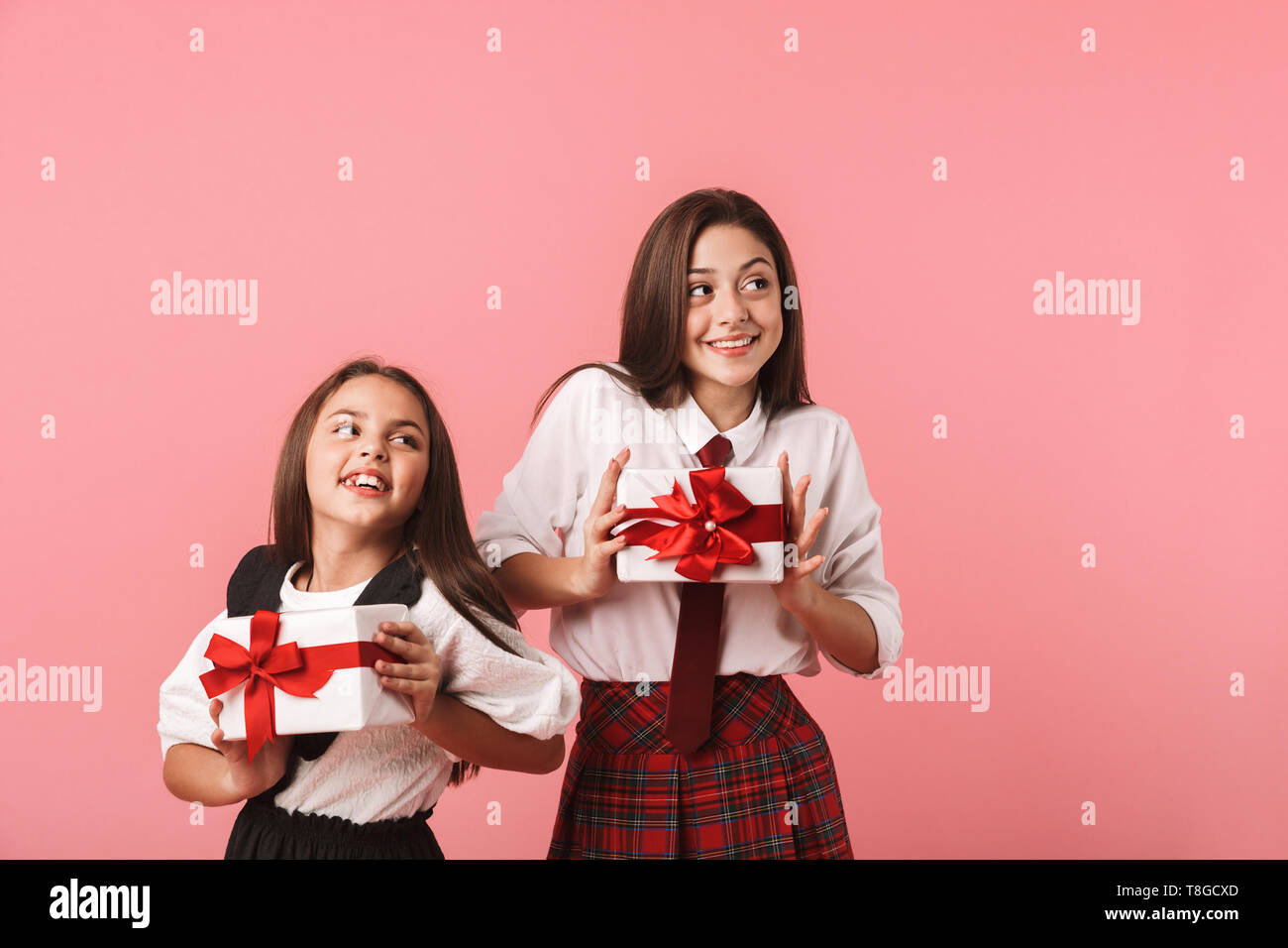 Ritratto di belle ragazze in uniforme scolastica tenendo presente le caselle mentre in piedi isolato su sfondo rosso Foto Stock