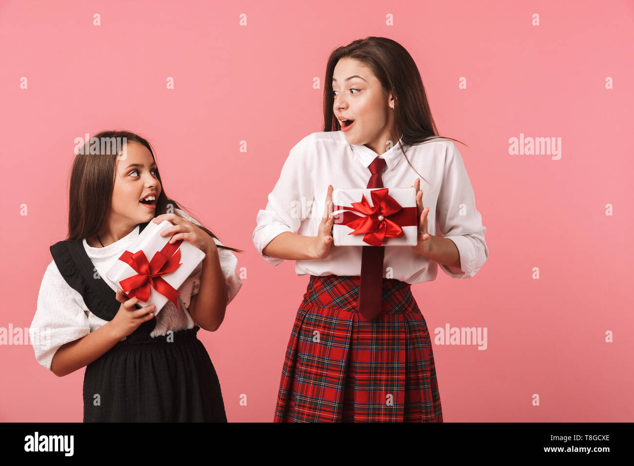 Ritratto di gioiosa ragazze in uniforme scolastica tenendo presente le caselle mentre in piedi isolato su sfondo rosso Foto Stock