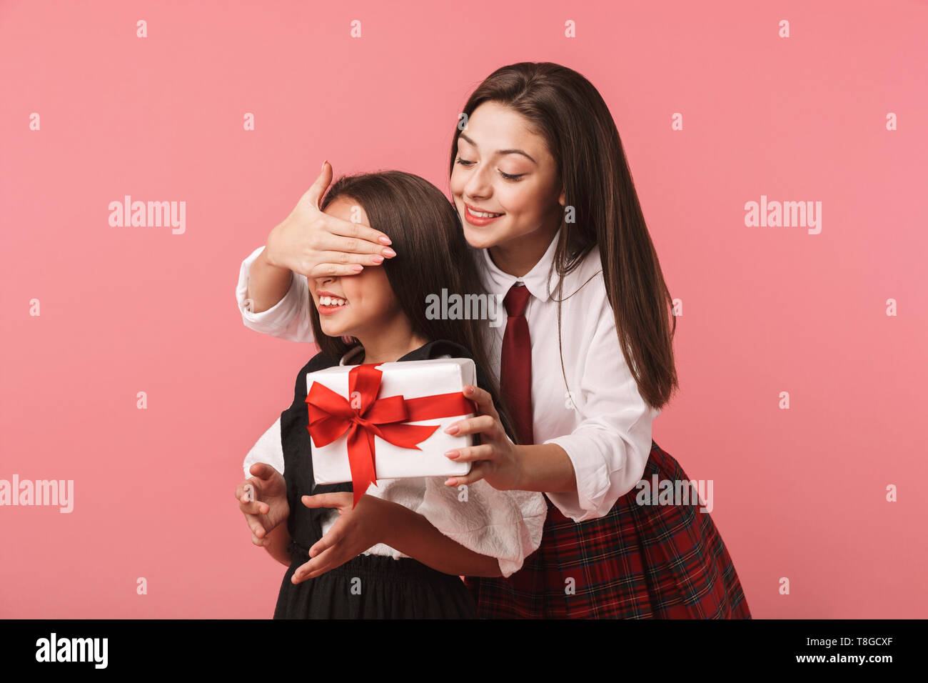 Ritratto di Allegro ragazze in uniforme scolastica azienda Scatole dono permanente, mentre isolate su sfondo rosso Foto Stock