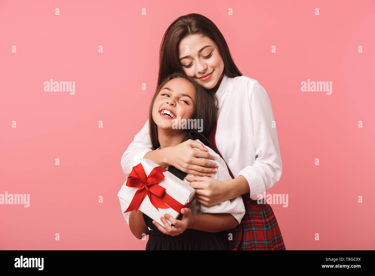 Ritratto di felice ragazze in uniforme scolastica azienda Scatole dono permanente, mentre isolate su sfondo rosso Foto Stock