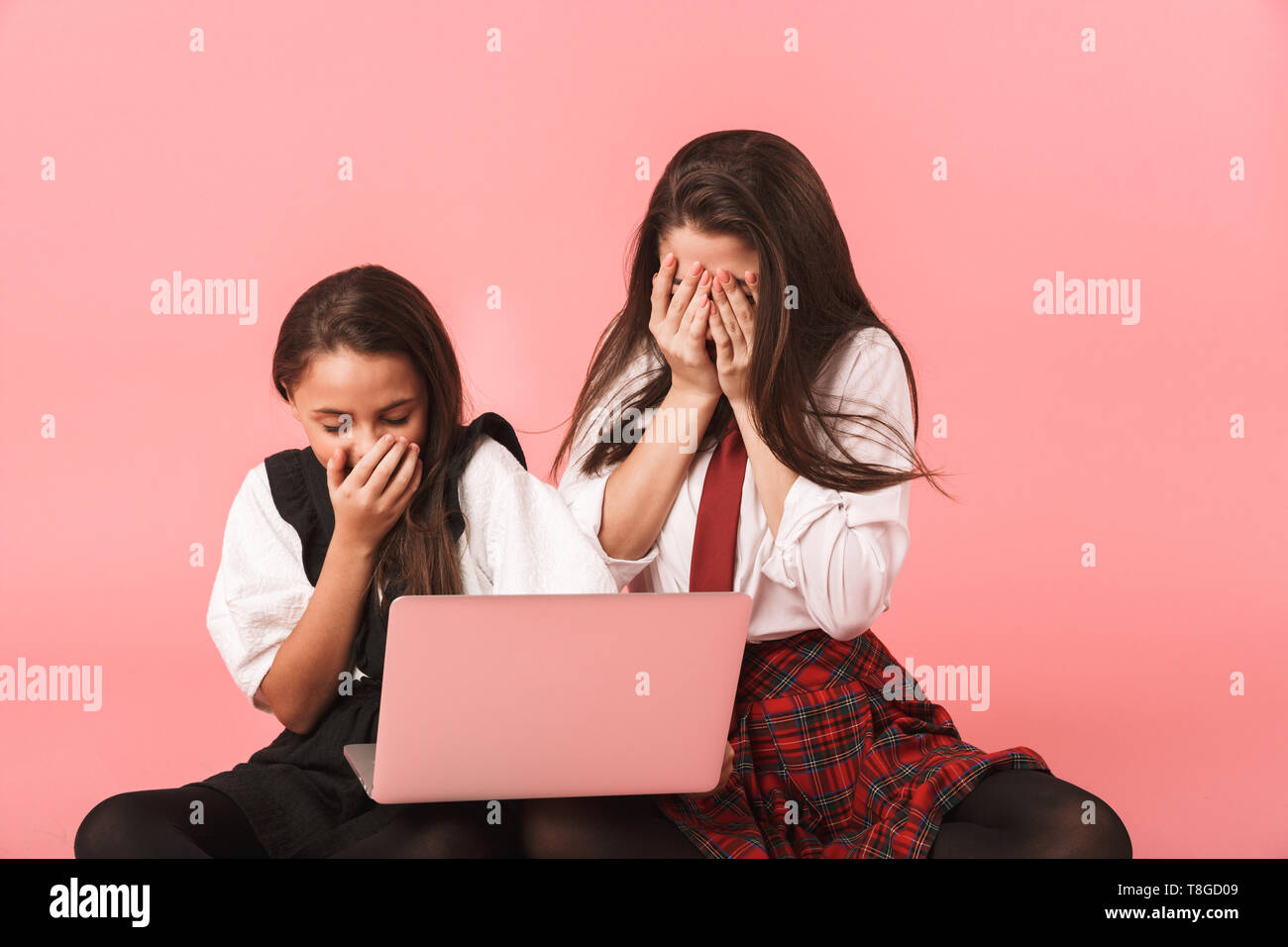 Ritratto di ragazze europeo in uniforme scolastica utilizzando computer portatile mentre è seduto sul pavimento isolato su sfondo rosso Foto Stock
