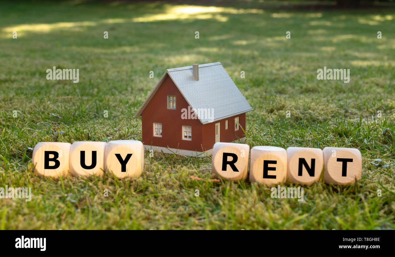 Concetto di acquisto o di affitto di una casa. Una casa in miniatura immessi sul prato verde. Dadi formano le parole 'ACQUISTA' e 'reNT'. Foto Stock
