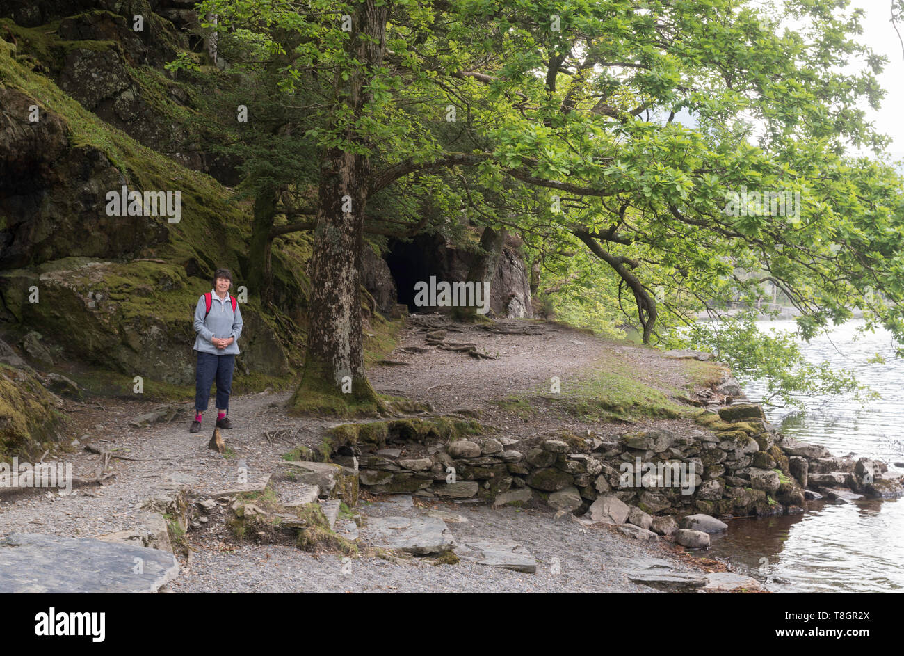 Donna anziana passeggiate intorno al lago di Buttermere con tunnel di roccia in background, Cumbria, England, Regno Unito Foto Stock