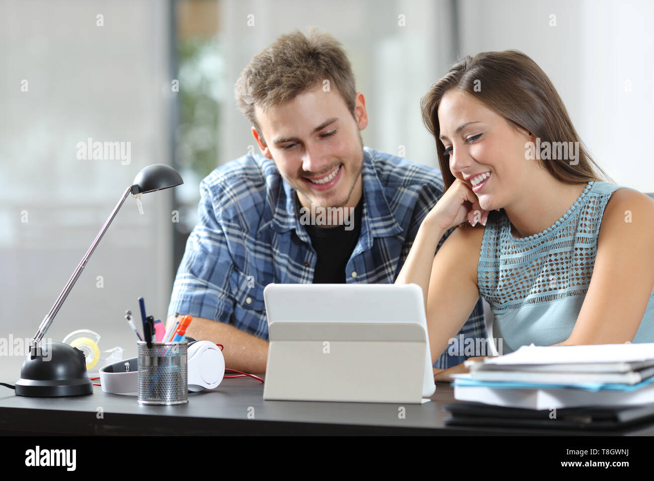 Coppia felice guardando tablet contenuti online seduto su una scrivania a casa Foto Stock