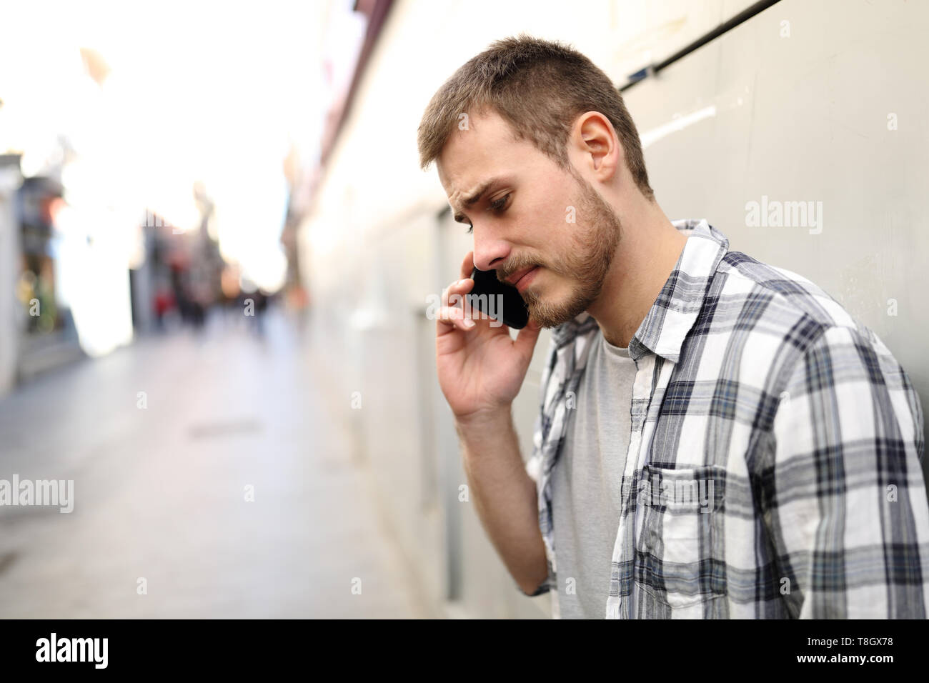 Vista laterale verticale di un triste uomo che parla al telefono da soli in una strada solitaria Foto Stock