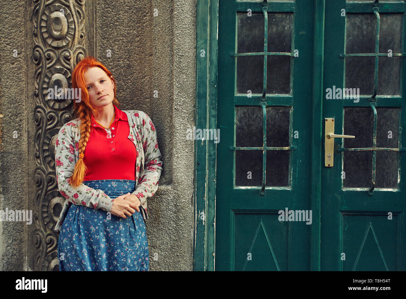Elegante donna informale in un mantello in prossimità di un edificio con una vecchia porta vintage Foto Stock