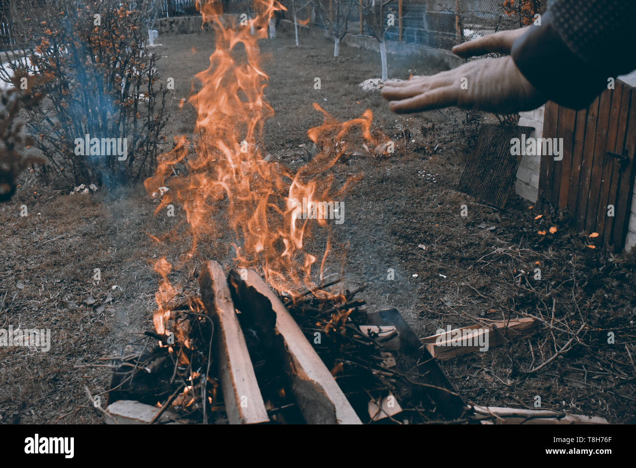 Uomo caucasico riscaldando le mani al campfire in una fredda atmosfera scura Foto Stock