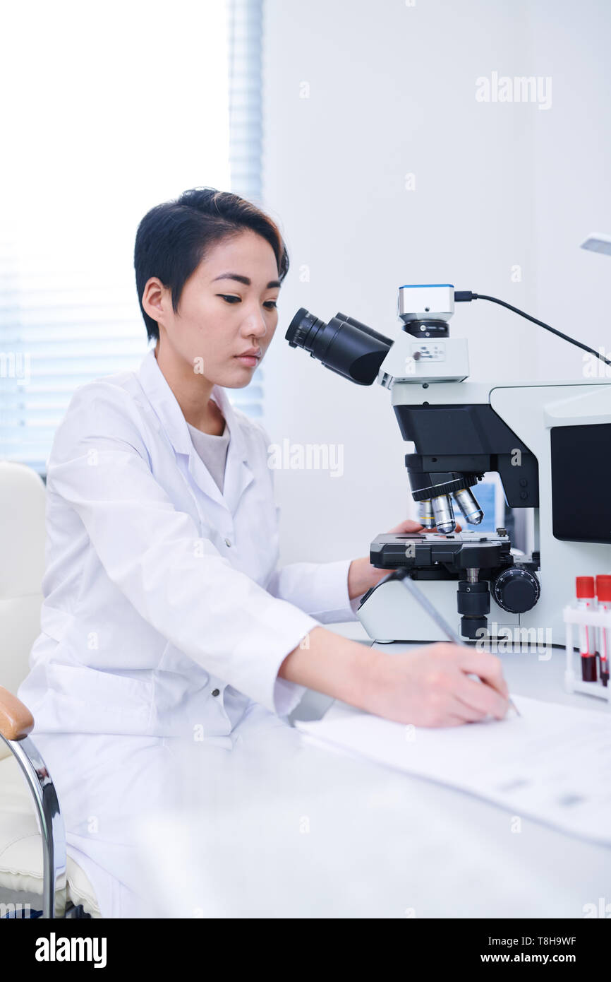 Biologo asiatici studiando le cellule con il microscopio Foto Stock