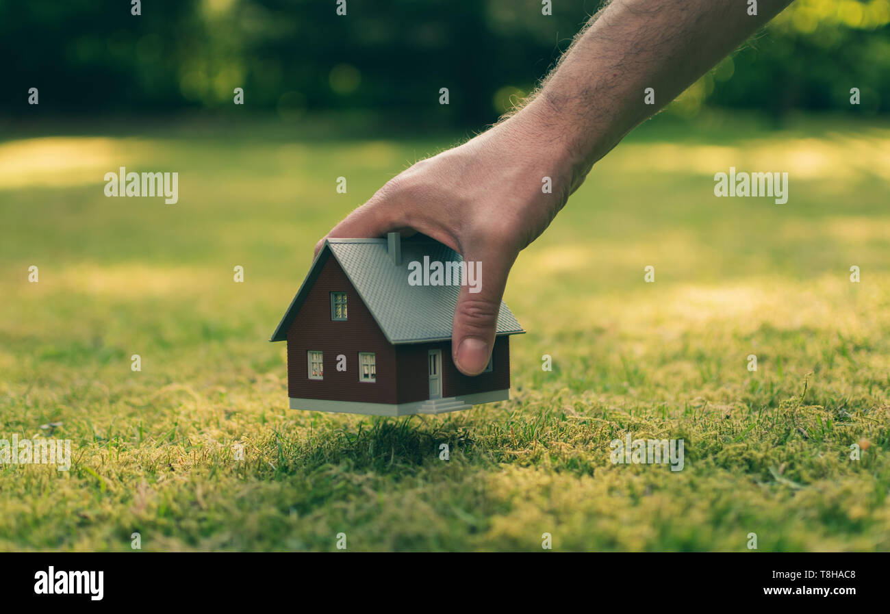 Concetto di vendita di una casa. Una mano è in possesso di un modello di casa sopra il verde prato. Foto Stock