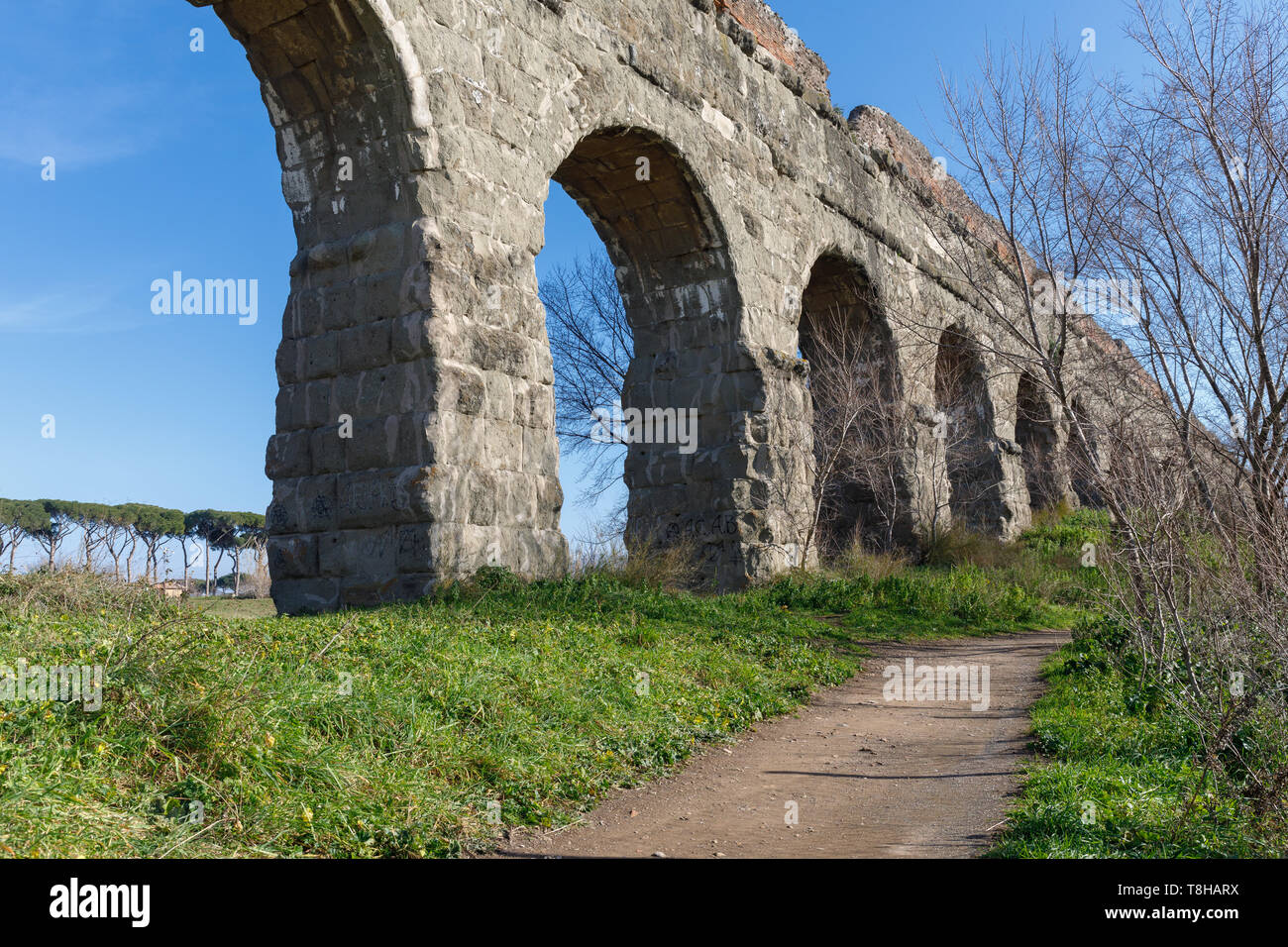 Arcate di un antico acquedotto romano, in blocchi di tufo. Il percorso si snoda lungo la proprietà in un parco verde nella periferia di Roma. Foto Stock