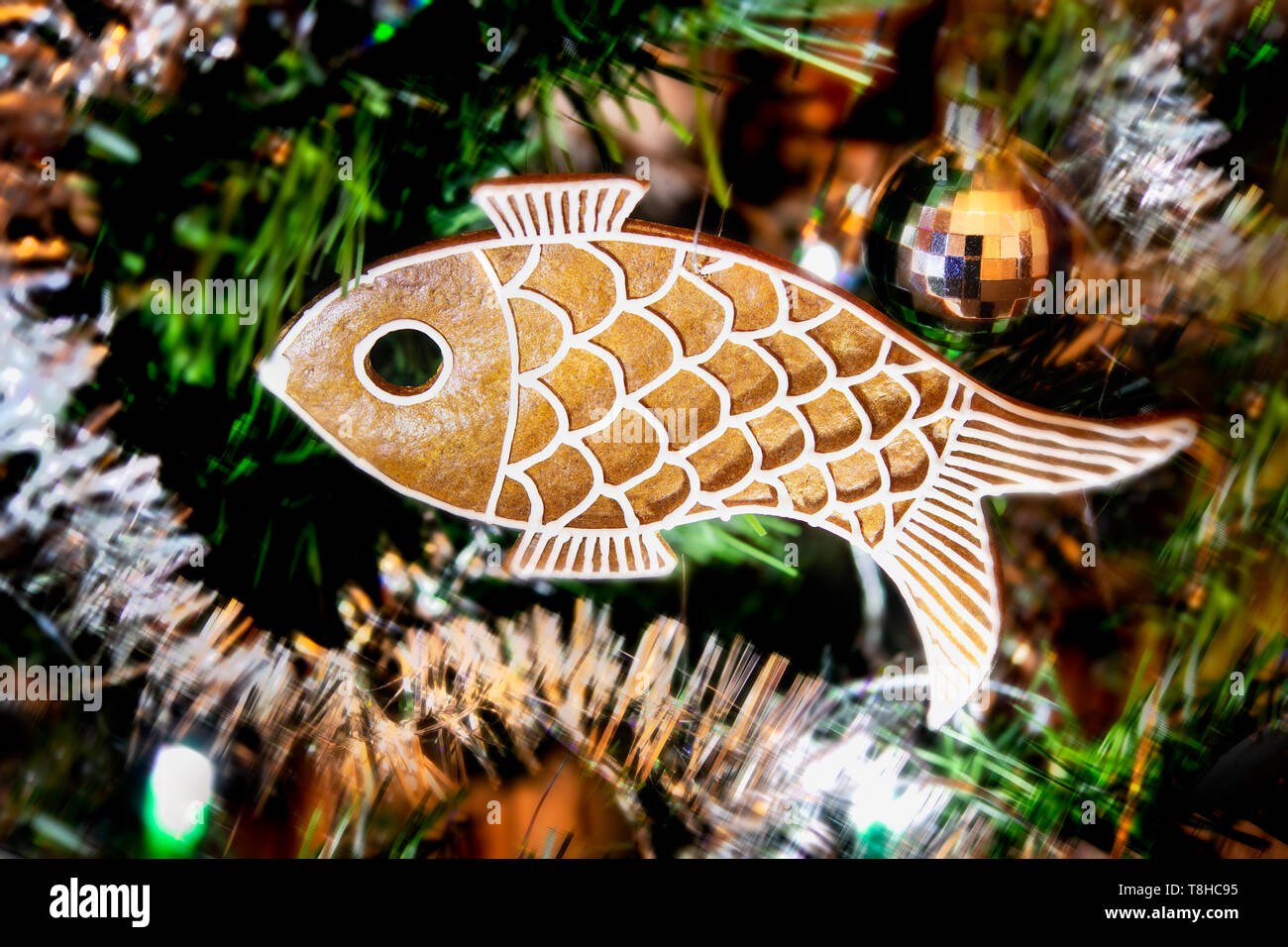 Dolce panpepato in forma di pesce sul pensile ornato albero di Natale. Fatte a mano cookie aromatico closeup sulla sfocatura dello sfondo verde di aghi. Xmas ghirlande. Foto Stock