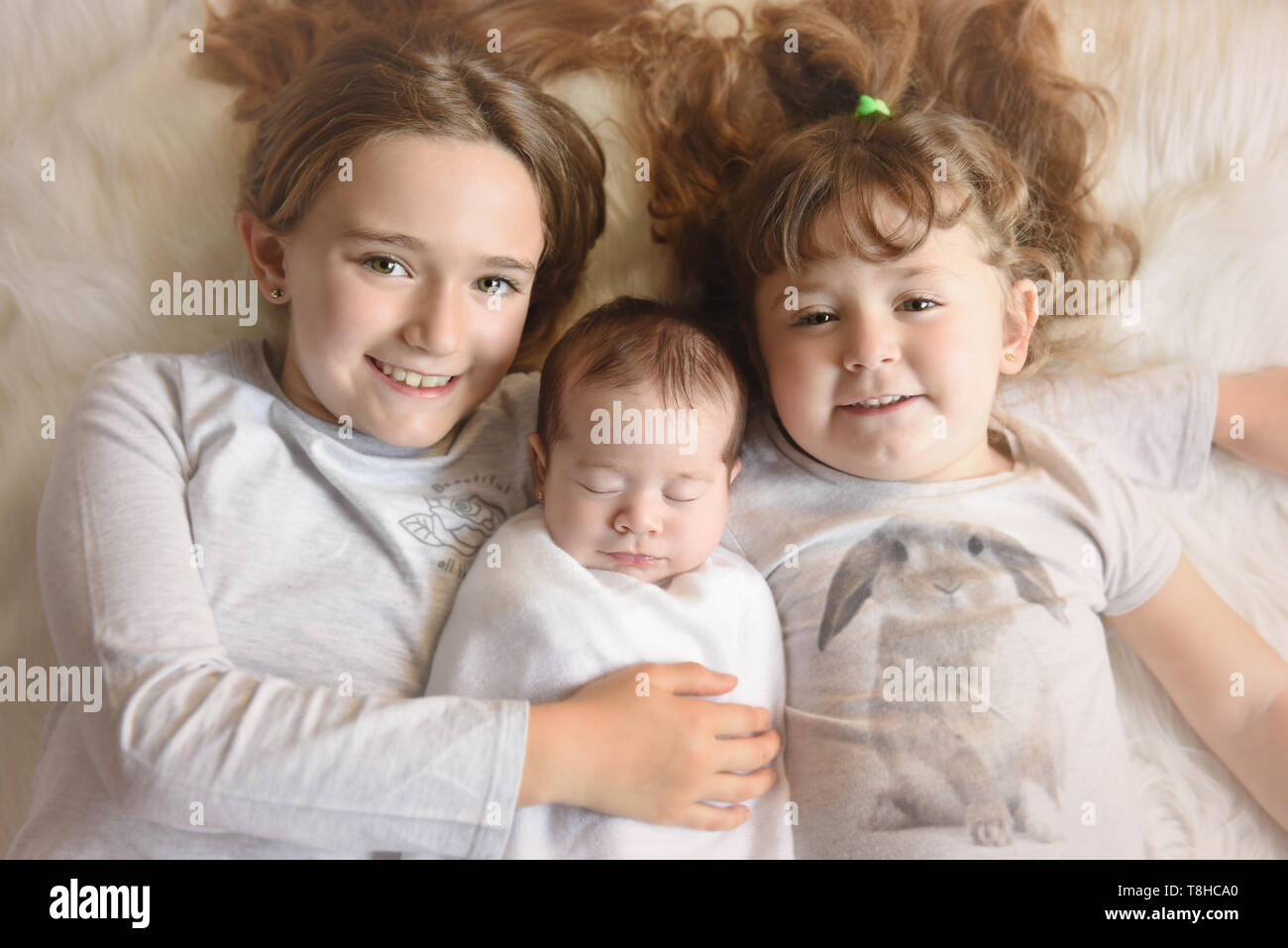 Due graziose sorelle holging il neonato sorella dorme Foto Stock