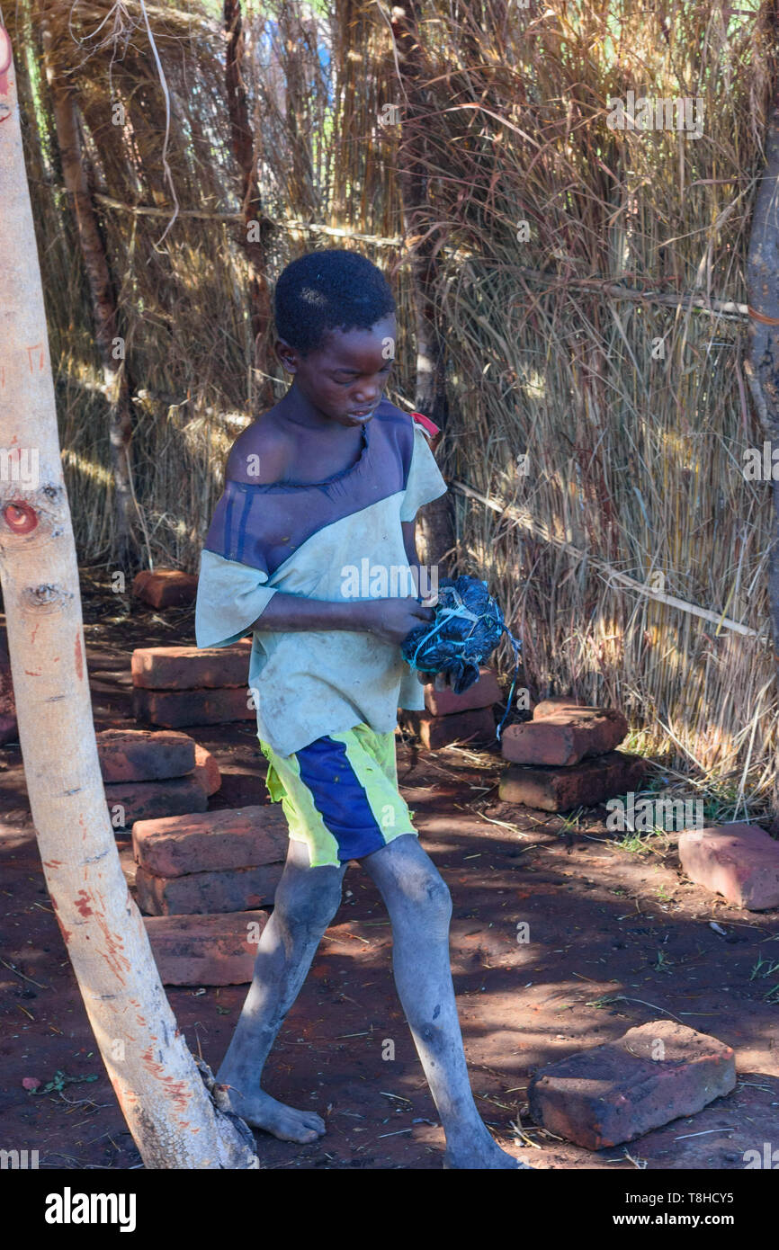 A piedi nudi sottile ragazzo del Malawi che indossano pantaloncini porta un calcio grezzo realizzata in sacchetti di plastica Foto Stock