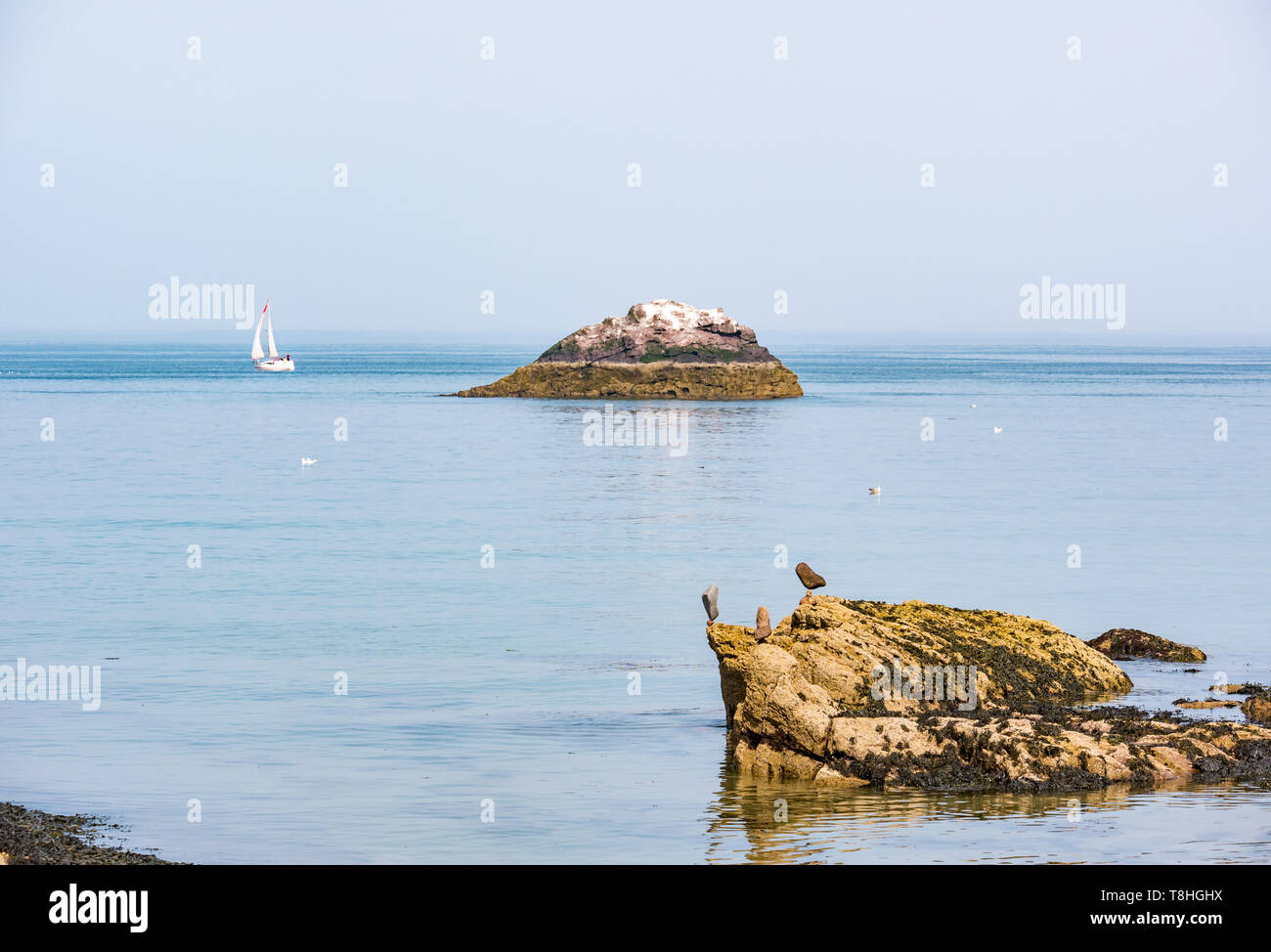 Pietre equilibrato sulla spiaggia rocciosa vicino al mare con barca a vela e isola, Firth of Forth, East Lothian, Scozia, Regno Unito Foto Stock