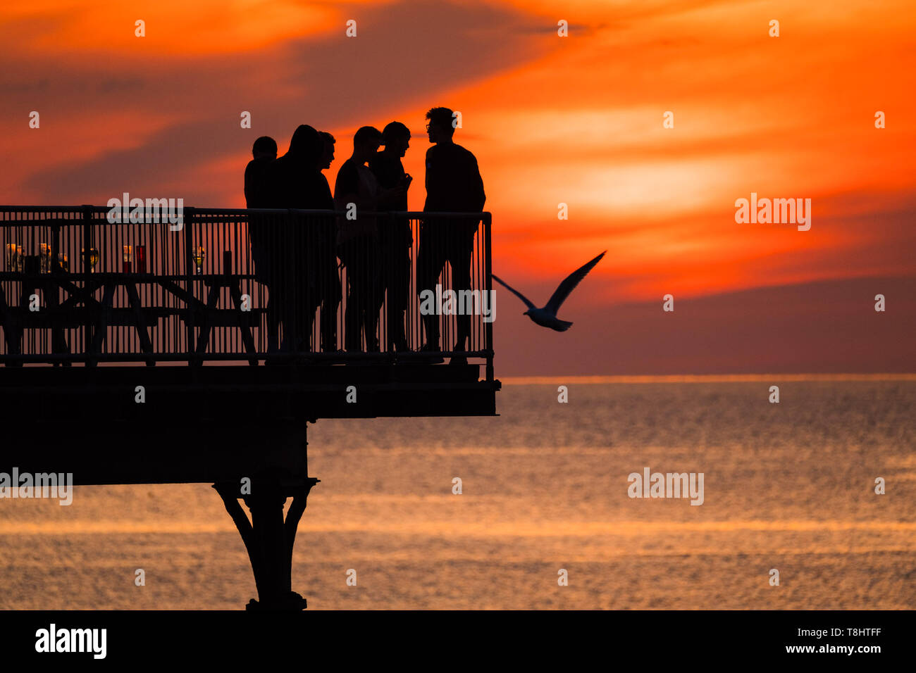 Aberystwyth Wales UK, lunedì 13 maggio 2019 UK Meteo: un gruppo di giovani uomini stagliano in piedi alla fine del molo godere guardando il glorioso tramonto dorato sulle acque di Cardigan Bay a Aberystwyth , portando a termine un giorno pf ininterrotte il caldo sole primaverile come un sistema di alta pressione domina il meteo in tutto il Regno Unito . Photo credit Keith Morris / Alamy Live News Foto Stock