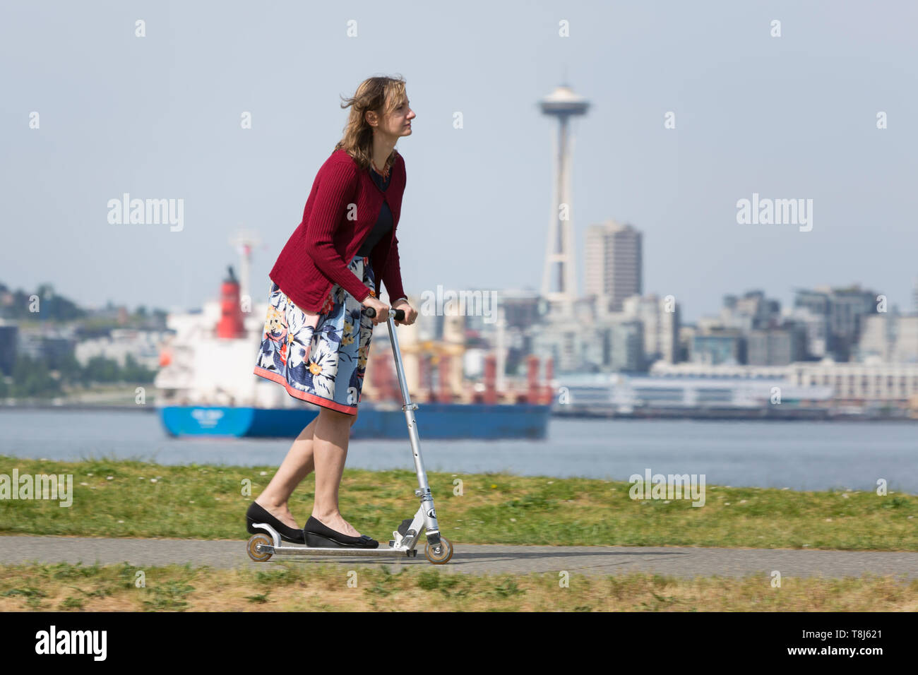 Seattle, Washington: una donna corse uno scooter lungo il sentiero di Alki nella zona ovest di Seattle. Foto Stock