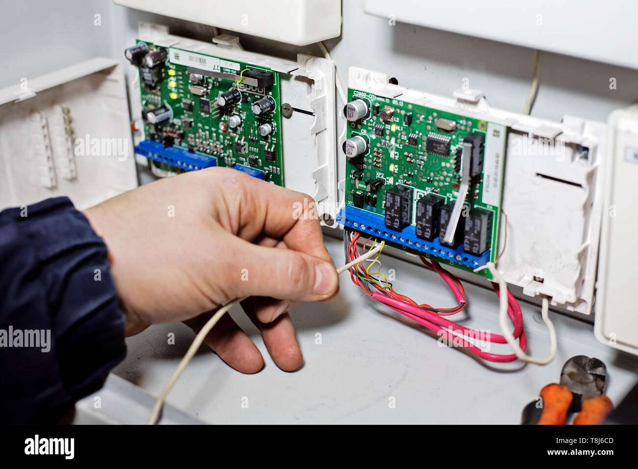 Una mano si collega il filo alla scheda a chip. Riparazione, manutenzione e regolazione di apparecchiature da parte di un tecnico qualificato. Sfondo Foto Stock