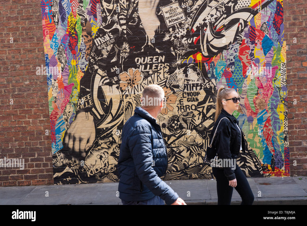 Uomo e donna che camminano accanto a un murales colorato su un muro di mattoni a York, North Yorkshire, Inghilterra Regno Unito. Foto Stock
