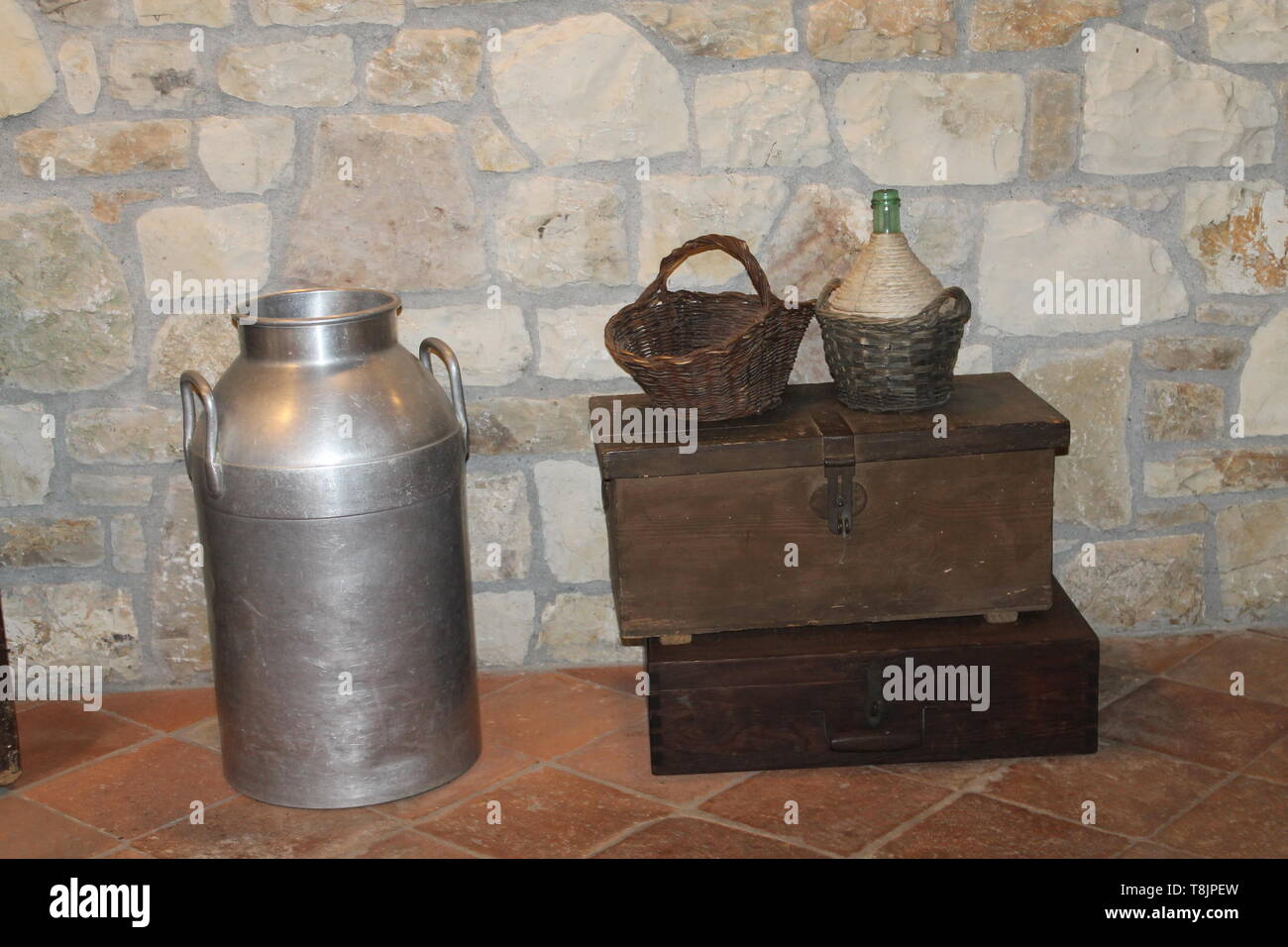 Strumenti rurali, cesto di vimini, bottiglia di vino e latte contenitore in acciaio Foto Stock