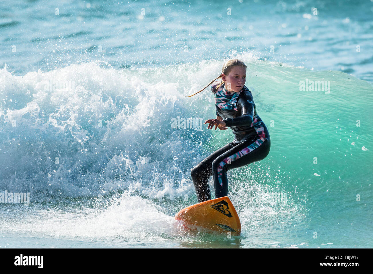 Spettacolare azione di surf come una giovane donna surfer cavalca un wave a Fistral a Newquay in Cornovaglia. Foto Stock