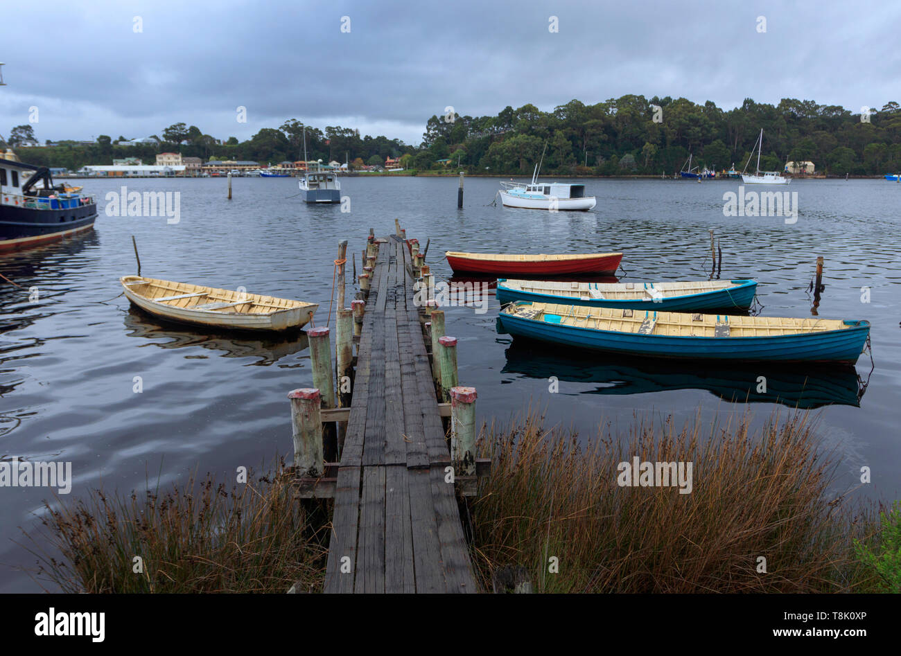 Barche di legno legata a un piccolo molo su Macquarie Harbour con la città di Strahan attraverso la baia in background. Foto Stock