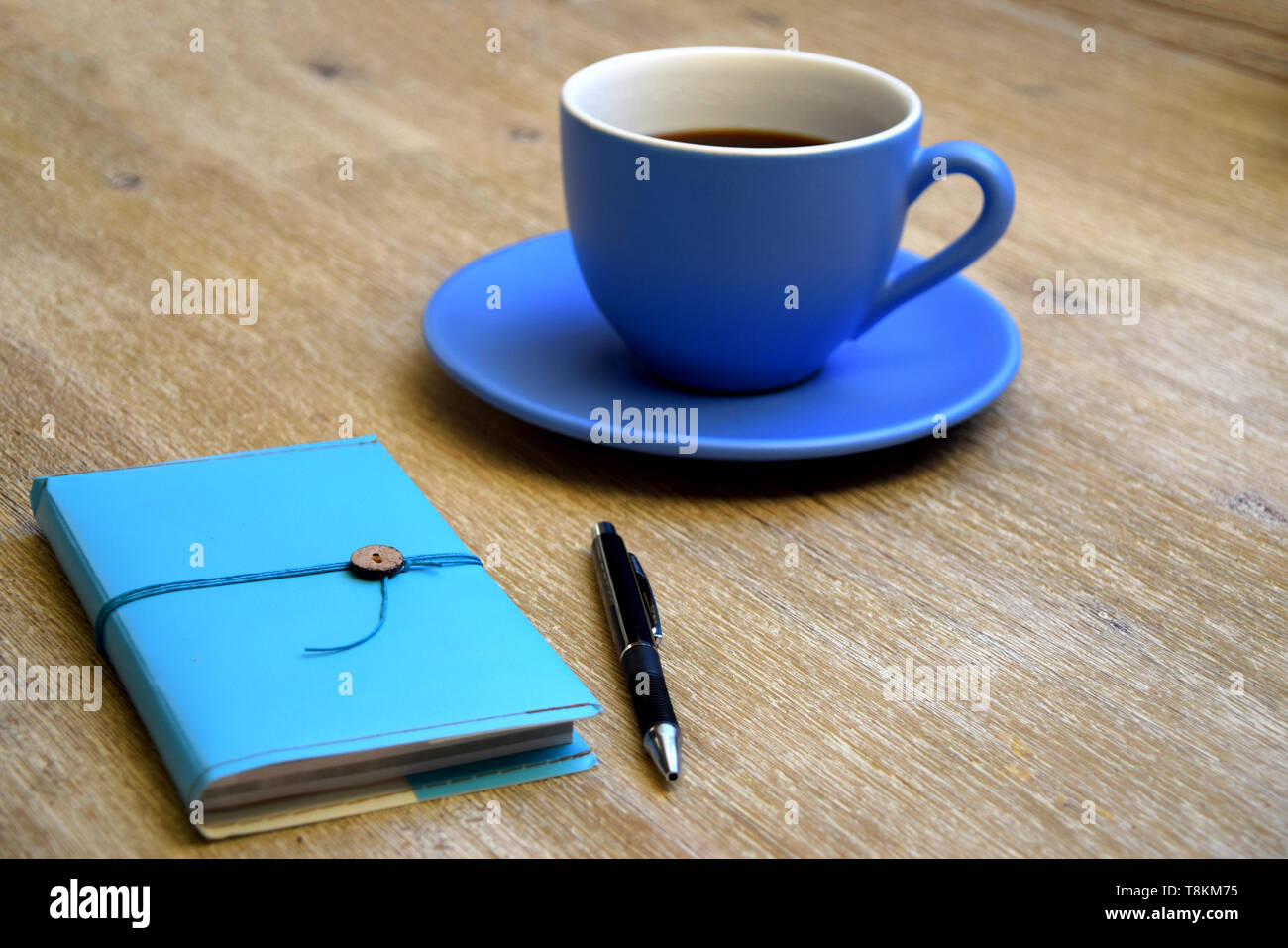Tazza di caffè, notebook blu e una penna su una tavola di legno Foto Stock