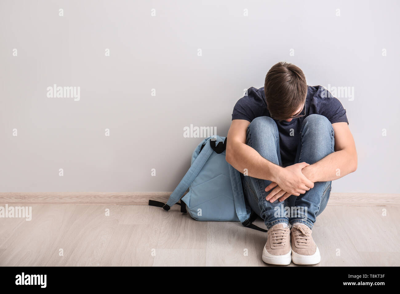 Triste ragazzo adolescente seduto sul pavimento in ambienti chiusi. Il bullismo a scuola Foto Stock