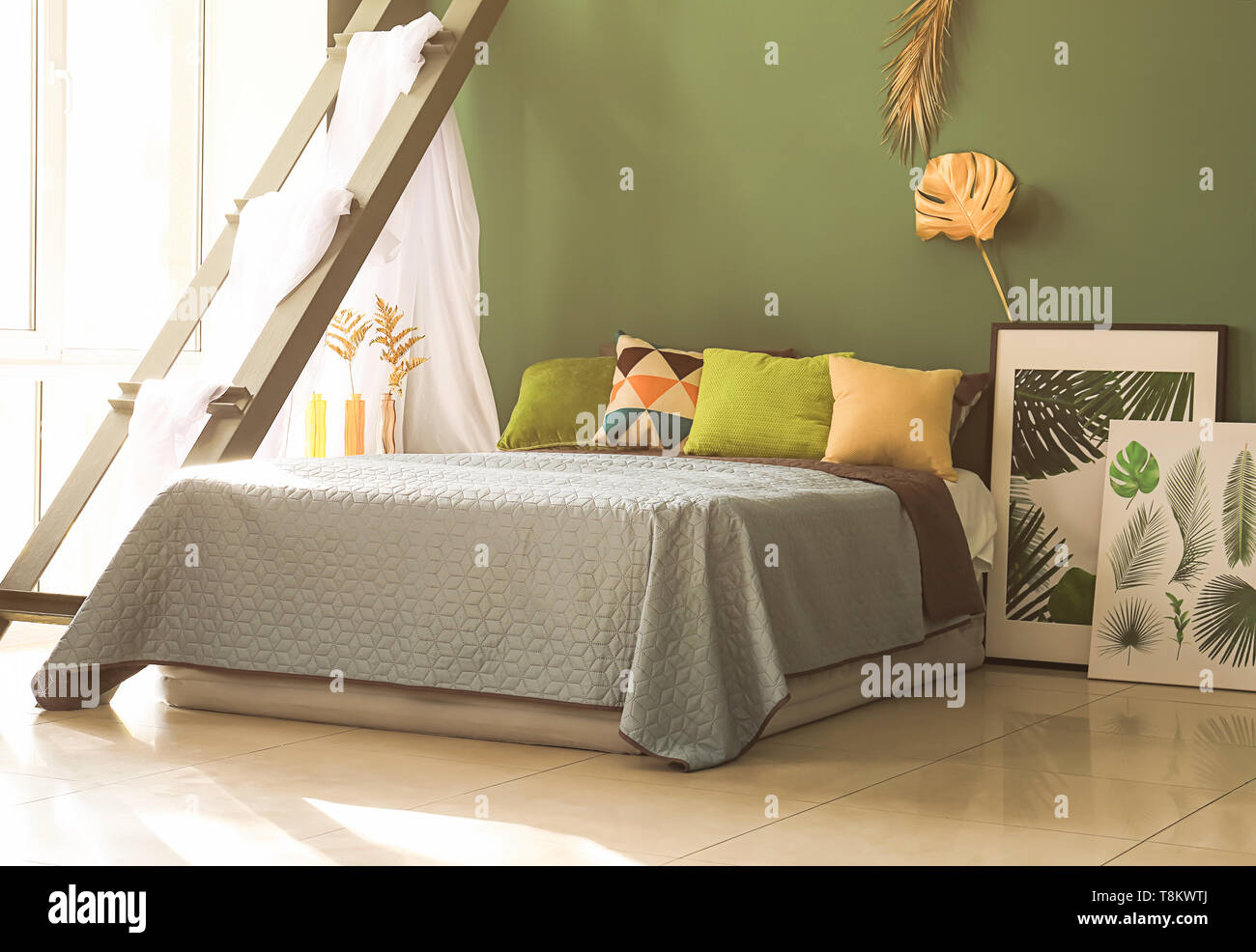 Interno del moderno e confortevole camera da letto con golden tropicale, lascia sulla parete del colore Foto Stock