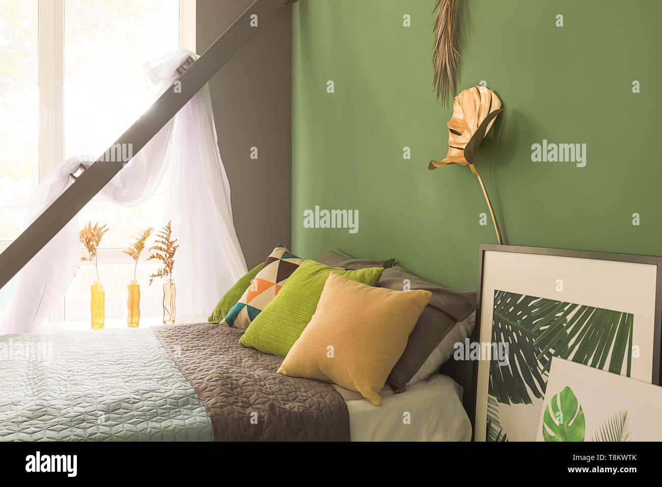 Interno del moderno e confortevole camera da letto con golden tropicale, lascia sulla parete del colore Foto Stock