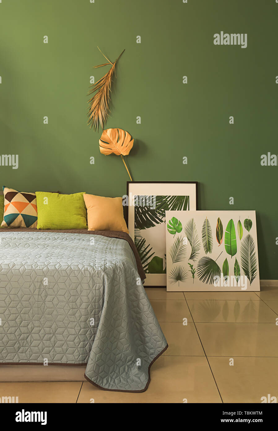 Interno del moderno e confortevole camera da letto con golden tropicale, lascia sulla parete del colore Foto Stock