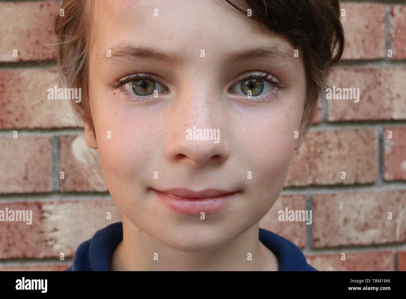 Ritratto di un bambino con grandi occhi verdi di fronte a un muro di mattoni Foto Stock