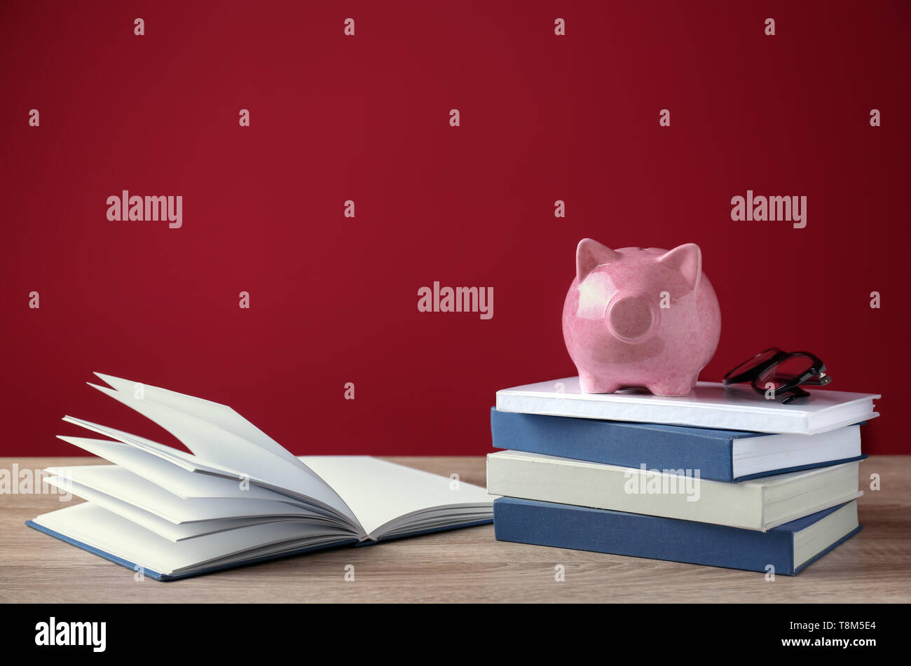 Carino salvadanaio sulla pila di libri contro il colore di sfondo Foto Stock