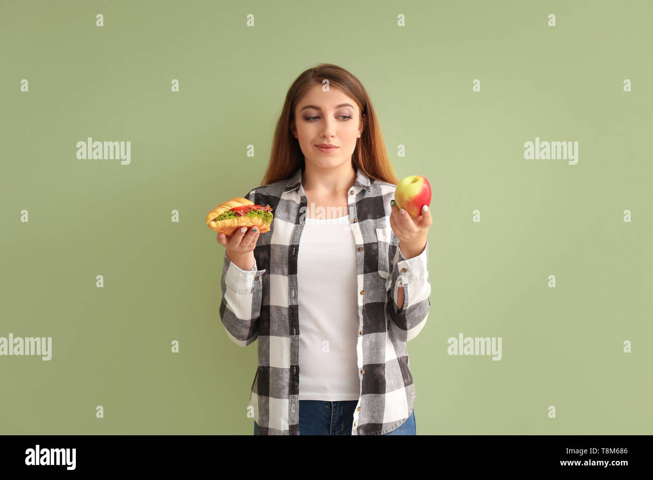 Giovane donna scegliendo tra un croissant e apple sul colore di sfondo Foto Stock