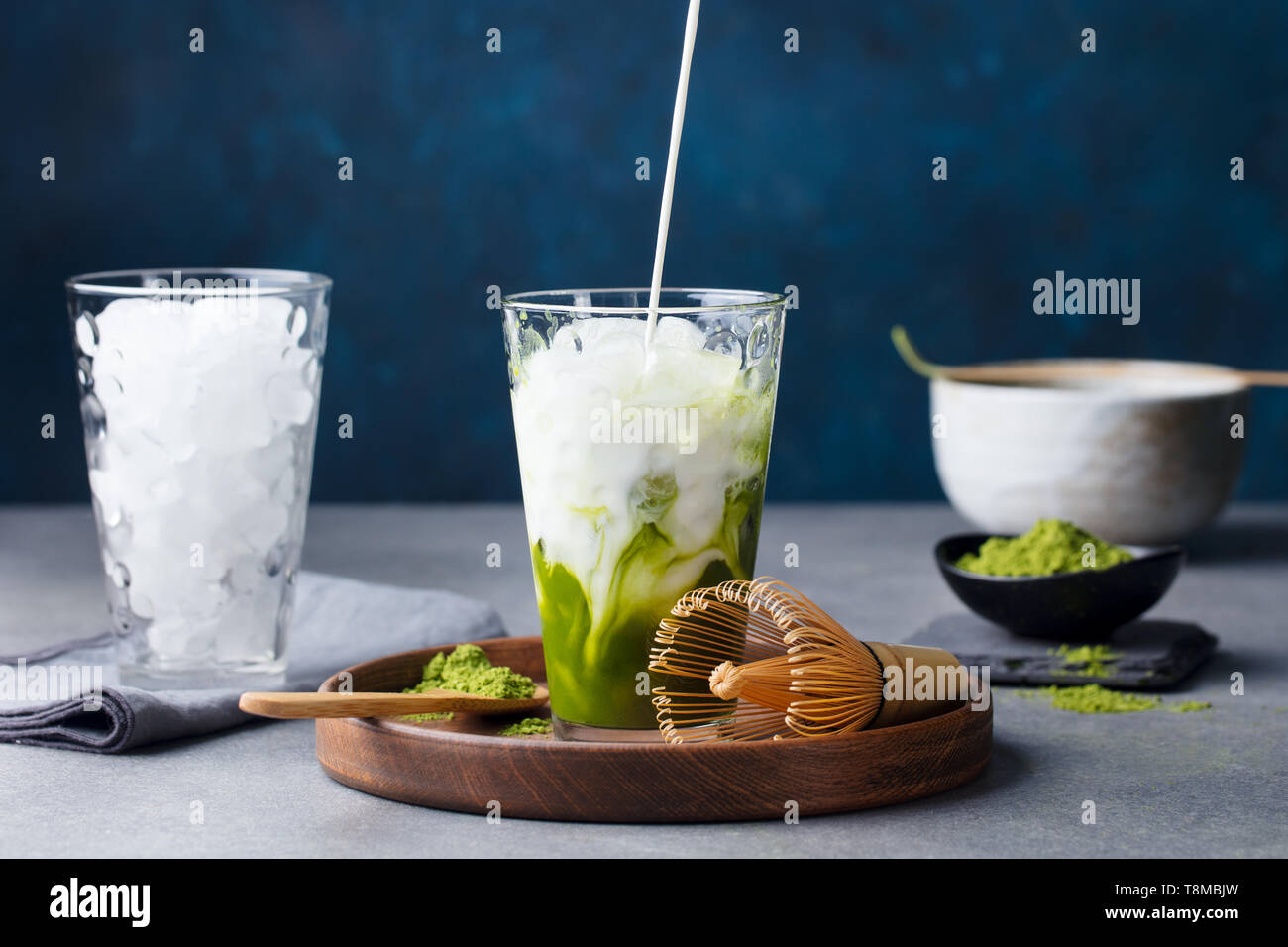 Matcha, il tè verde ice tea versando nel bicchiere alto sul piatto di legno. Grigio pietra dello sfondo. Foto Stock