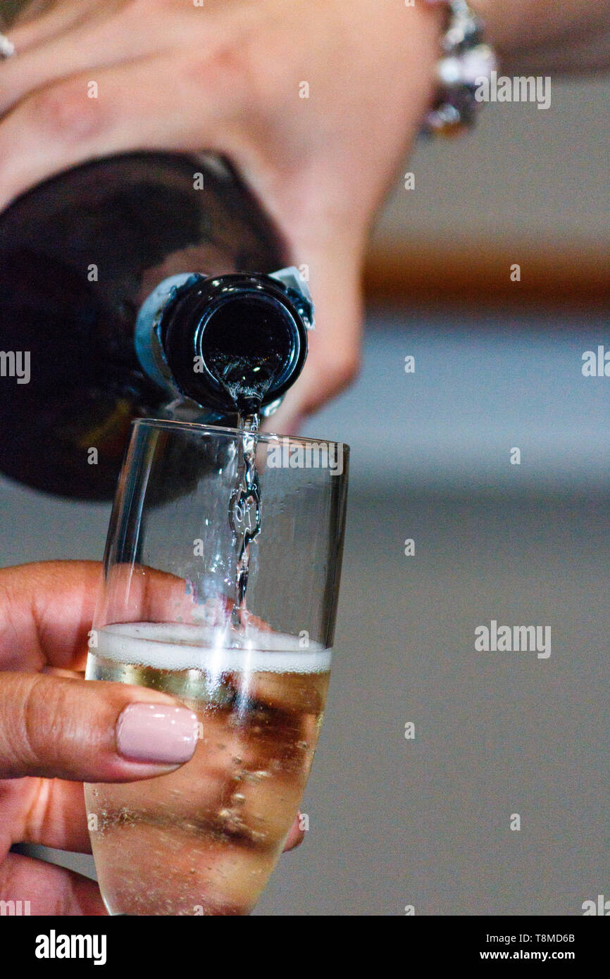Barista versando champagne in un bicchiere tenuto da una donna. Foto Stock