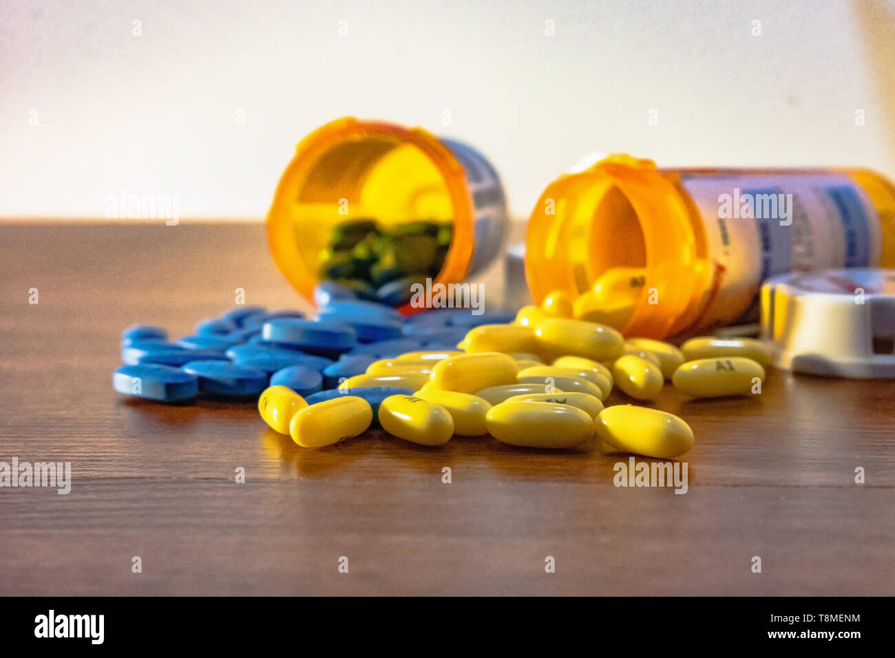 Due bottiglie di prescrizione ribaltato con il giallo e il blu pillole riversandosi su tavola. Pillole sono a fuoco con le bottiglie al di fuori della messa a fuoco. Foto Stock