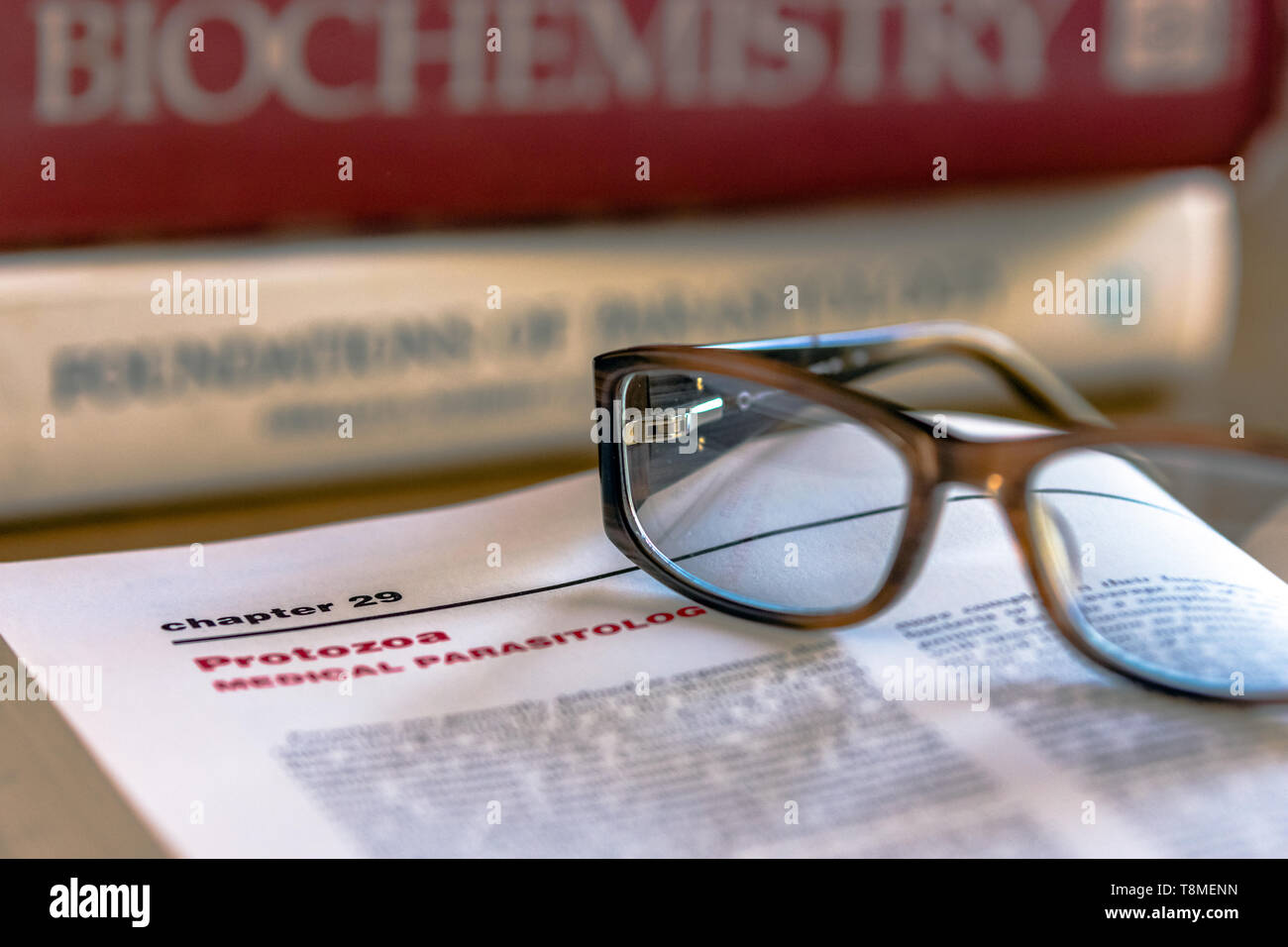 Occhiali sulla parte superiore di un libro aperto con i protozoi Medical Parassitologia a fuoco con altre scienze della vita i libri di testo in background al di fuori della messa a fuoco Foto Stock