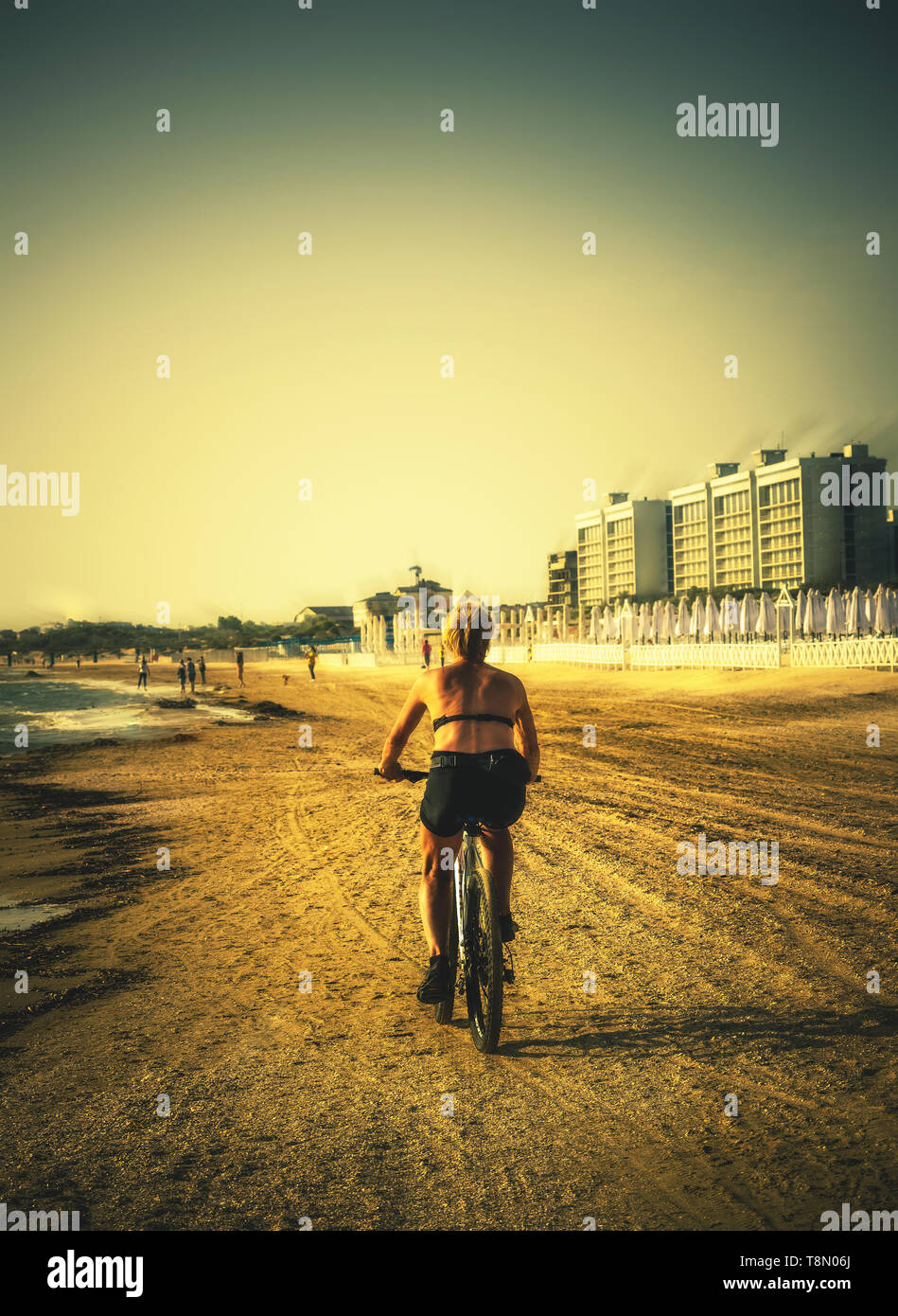 Donna anziana correre in bici lungo la spiaggia Foto Stock