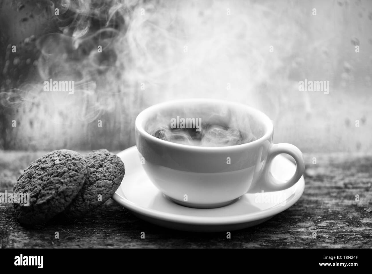 Bevanda al caffè con biscotti di avena dessert. Godendo del caffè sulla giornata di pioggia. Tempo di caffè sul giorno di pioggia. Caffe' macinato di fresco in bianco tazza o tazza alta sul davanzale. Wet vetro della finestra e la tazza di caffeina calda bevanda. Foto Stock