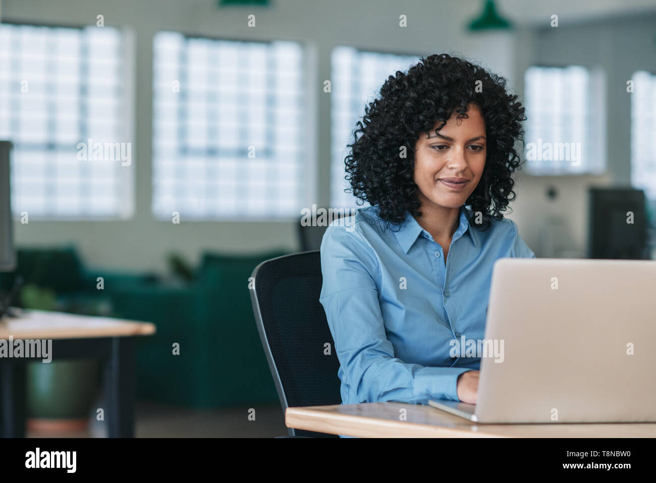 Imprenditrice sorridente seduto alla sua scrivania che lavora su un notebook Foto Stock