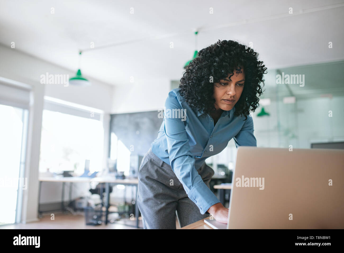 Focalizzato imprenditrice appoggiata sulla sua scrivania da ufficio con un notebook Foto Stock